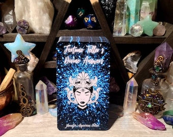 May include: A deck of blue and silver tarot cards with a sparkly background. The cards feature a woman with a third eye and a crown. The text on the cards reads "Fortune Teller's Divine Answers" and "Jennifer Aquarius Tarot".