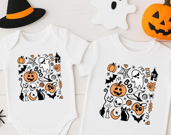 May include: White baby bodysuit and t-shirt with a Halloween-themed design. The design includes orange pumpkins, a black cat, a witch's hat, and the word "BOO". Decorative spiders, a ghost, and a jack-o'-lantern complete the festive scene.