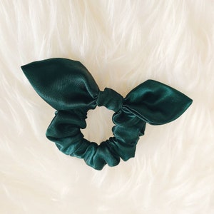 May include: A dark green satin scrunchie with a bow on top.