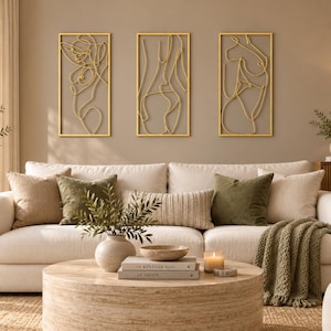 May include: A set of three rectangular wall art pieces featuring gold-toned wire outlines of human figures. Each piece is framed in a thin gold border, showcasing continuous line art designs that depict abstract silhouettes of the human form.