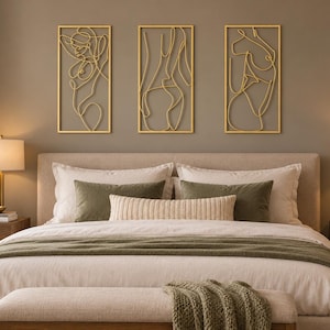 May include: Three rectangular gold-colored metal wall art pieces featuring continuous line drawings of human figures. Each piece is framed in a thin gold border and displays a stylized, abstract outline of a body in a minimalist wire design.