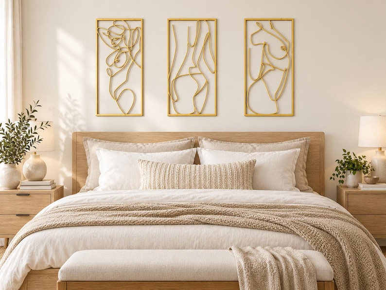 May include: Three rectangular wall art pieces featuring gold-toned wire outlines of human figures. Each piece is framed in a thin gold border, displaying continuous line art of abstract bodies mounted horizontally above a wooden bed frame.