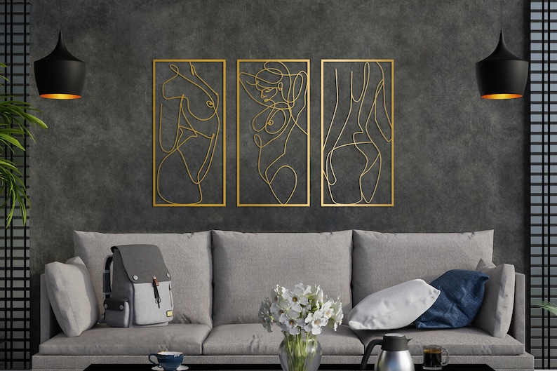 May include: A set of three rectangular gold-colored metal wall art pieces featuring continuous line drawings of human figures. Each piece is framed in a thin gold border, showcasing abstract silhouettes of the torso and body in a minimalist style.