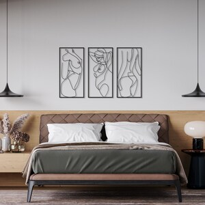 May include: A set of three rectangular black metal wall art pieces featuring continuous line drawings of human figures. Each piece is framed in a thin black border and displays a distinct abstract silhouette of a body in a single black line.