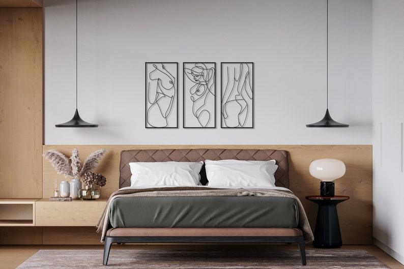May include: A set of three rectangular black metal wall art pieces featuring continuous line drawings of human figures. Each piece is framed in a thin black border and displays a distinct abstract silhouette of a body in a single black line.