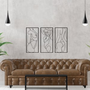 May include: A set of three rectangular black metal wall art pieces featuring continuous line drawings of human figures. Each piece is framed in a thin black border, showcasing abstract silhouettes of the body in a minimalist black wire design.