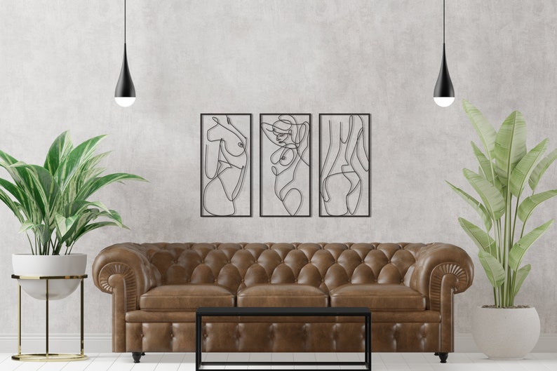 May include: A set of three rectangular black metal wall art pieces featuring continuous line drawings of human figures. Each piece is framed in a thin black border, showcasing abstract silhouettes of the body in a minimalist black wire design.