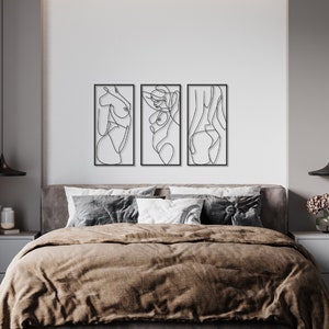 May include: A set of three rectangular black metal wall art pieces featuring continuous line drawings of human figures. Each piece is framed in a thin black border and displays a distinct abstract silhouette of a body in a single black line.