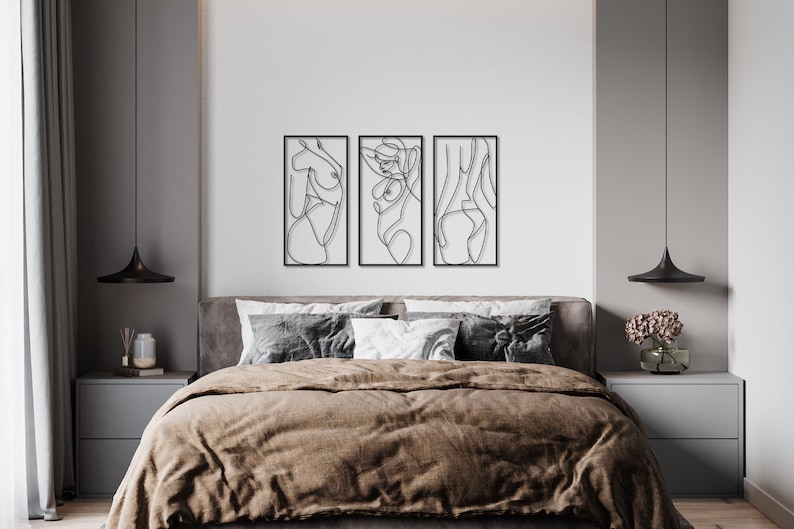 May include: A set of three rectangular black metal wall art pieces featuring continuous line drawings of human figures. Each piece is framed in a thin black border and displays a distinct abstract silhouette of a body in a single black line.