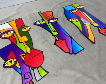 May include: Three abstract colorful face sculptures with geometric shapes and bold lines. The sculptures are made of metal and have a glossy finish. The colors include red, yellow, green, blue, purple, and orange.