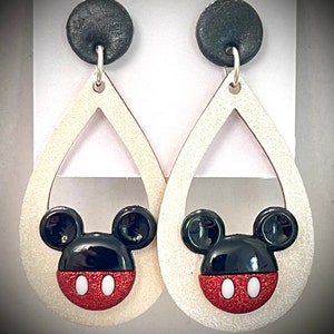 May include: A pair of dangle earrings with a white teardrop-shaped base and a black and red Mickey Mouse head design. The earrings have black tops.