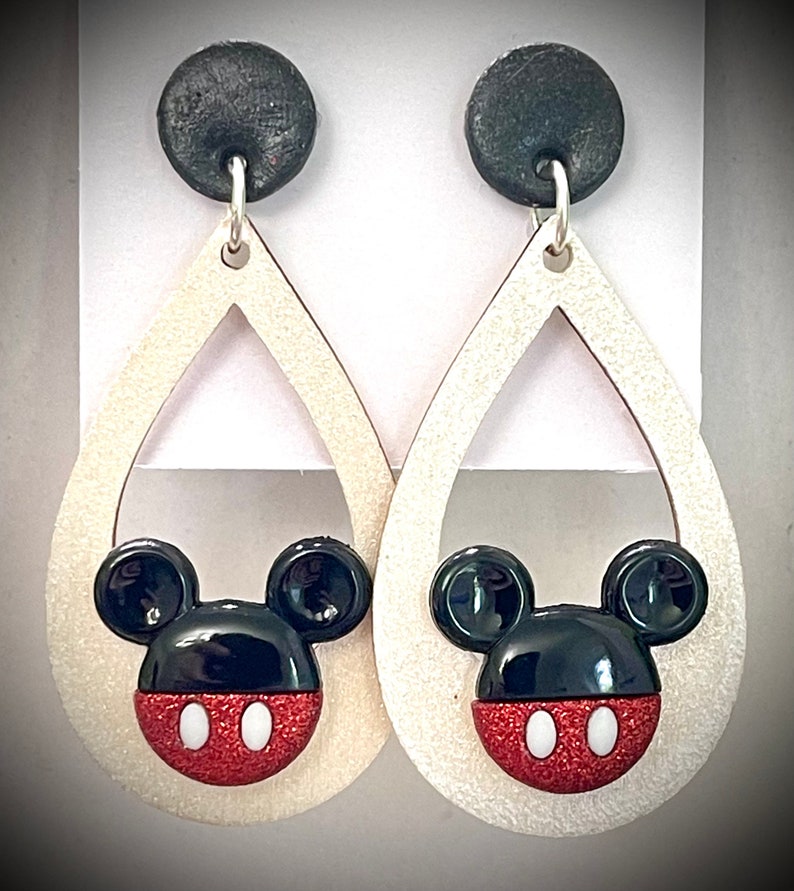 May include: A pair of dangle earrings with a white teardrop-shaped base and a black and red Mickey Mouse head design. The earrings have black tops.