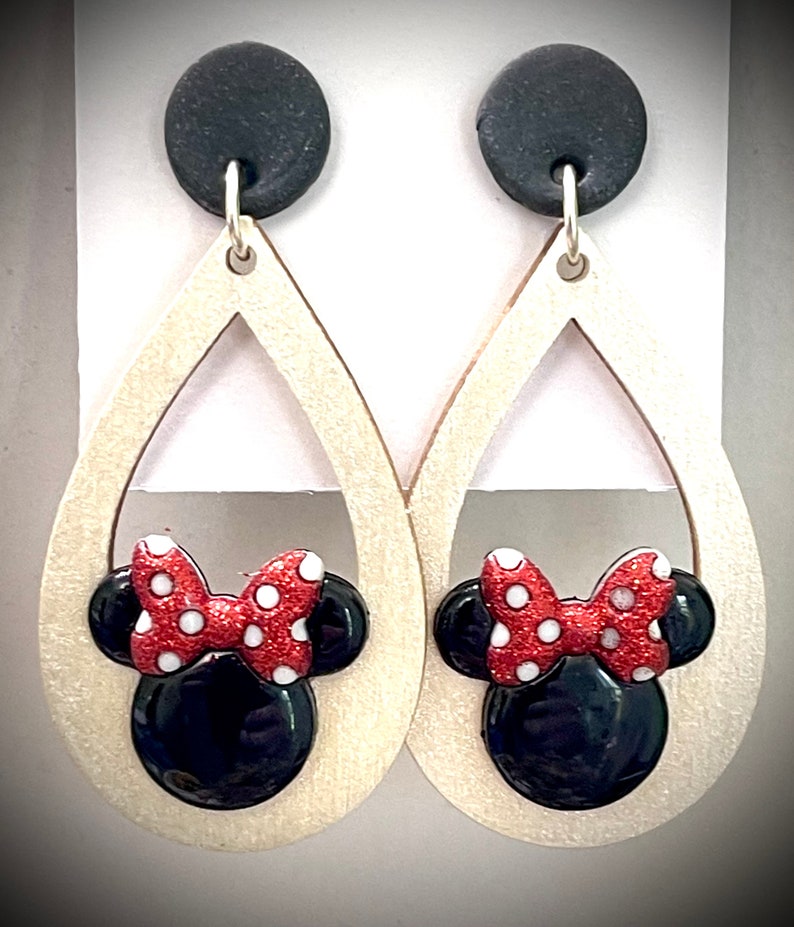 May include: A pair of dangle earrings with a wooden teardrop shape and a black and red Minnie Mouse head design. The earrings have black clay tops.