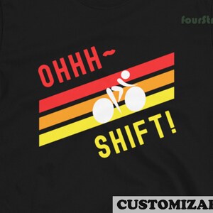 Könnte beinhalten: Schwarzes T-Shirt mit einem Retro-Design, das einen Radfahrer auf einem Fahrrad mit dem Text "OHHH-SHIFT!" in Rot und Gelb zeigt.