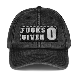 Könnte beinhalten: Eine schwarze, abgenutzte Baseballkappe aus Denim mit einem weißen gestickten Aufnäher, auf dem "F*CKS GIVEN 0" steht.