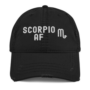 May include: Black distressed baseball cap with white embroidered text "Scorpio AF" and the astrological symbol for Scorpio.
