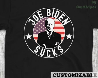 May include: Black t-shirt with a white circle graphic featuring a caricature of Joe Biden with the text "Joe Biden Sucks" and an American flag in the background.