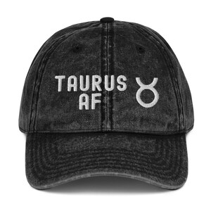 May include: Black distressed denim baseball cap with white embroidered text "Taurus AF" and a Taurus zodiac symbol.