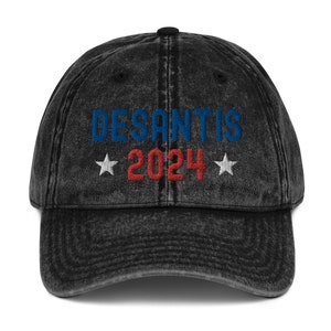 Puede incluir: Una gorra de béisbol negra de estilo vintage con el texto "DESANTIS 2024" bordado en azul, rojo y blanco.