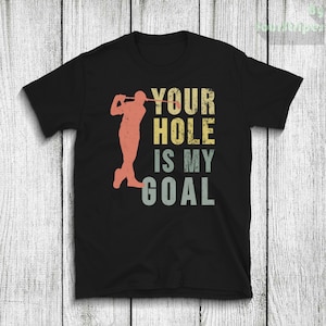 Puede incluir: Camiseta negra con un gráfico de estilo vintage de un golfista y el texto "Your Hole Is My Goal".