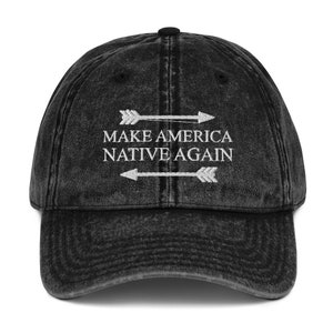May include: A black vintage washed denim baseball cap with white embroidery that reads "Make America Native Again" with two arrows pointing in opposite directions.