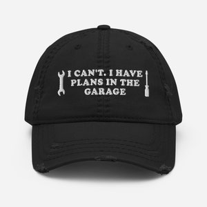 May include: Black distressed baseball cap with white embroidery that reads "I can't. I have plans in the garage."  The embroidery also includes a wrench and a screwdriver.