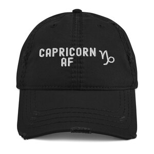 Könnte beinhalten: Schwarze Baseballkappe mit Used-Look und weiß gesticktem Text "CAPRICORN AF" sowie einem Steinbock-Symbol. Die Kappe hat einen gebogenen Schirm und einen Vintage-Look.