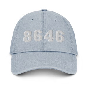 Puede incluir: Una gorra de b&eacute;isbol de denim azul claro con el n&uacute;mero "8646" bordado en blanco en la parte delantera.