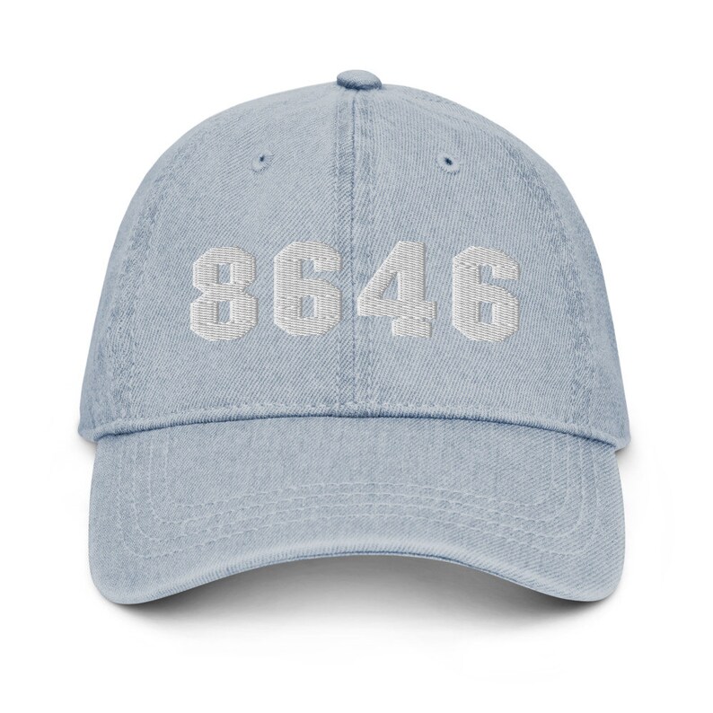 Puede incluir: Una gorra de b&eacute;isbol de denim azul claro con el n&uacute;mero "8646" bordado en blanco en la parte delantera.