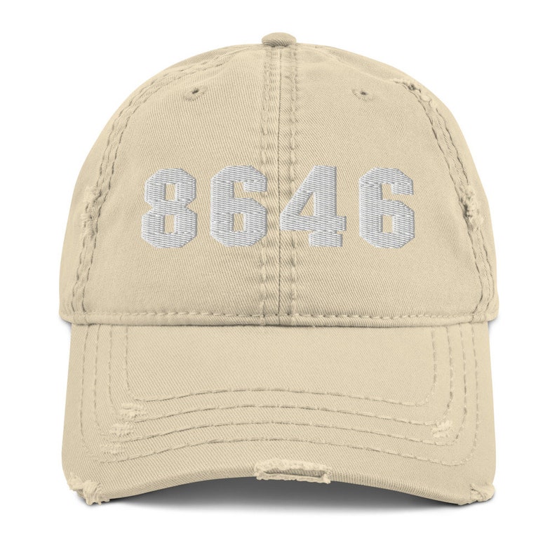 May include: A beige distressed baseball cap with the number 8646 embroidered in white on the front.
