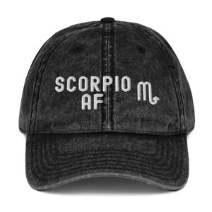 May include: Black distressed denim baseball cap with white embroidered text "Scorpio AF" and the astrological symbol for Scorpio.