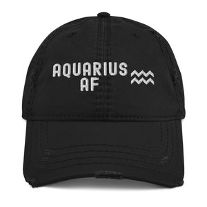 Könnte beinhalten: Schwarze, abgenutzte Baseballkappe mit weiß gesticktem Text "Aquarius AF" und dem astrologischen Symbol des Wassermanns.
