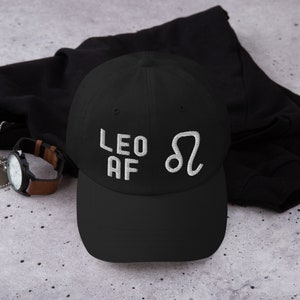 Könnte beinhalten: Schwarze Baseballkappe mit weiß gesticktem Text "Leo AF" und dem astrologischen Symbol für Löwe.