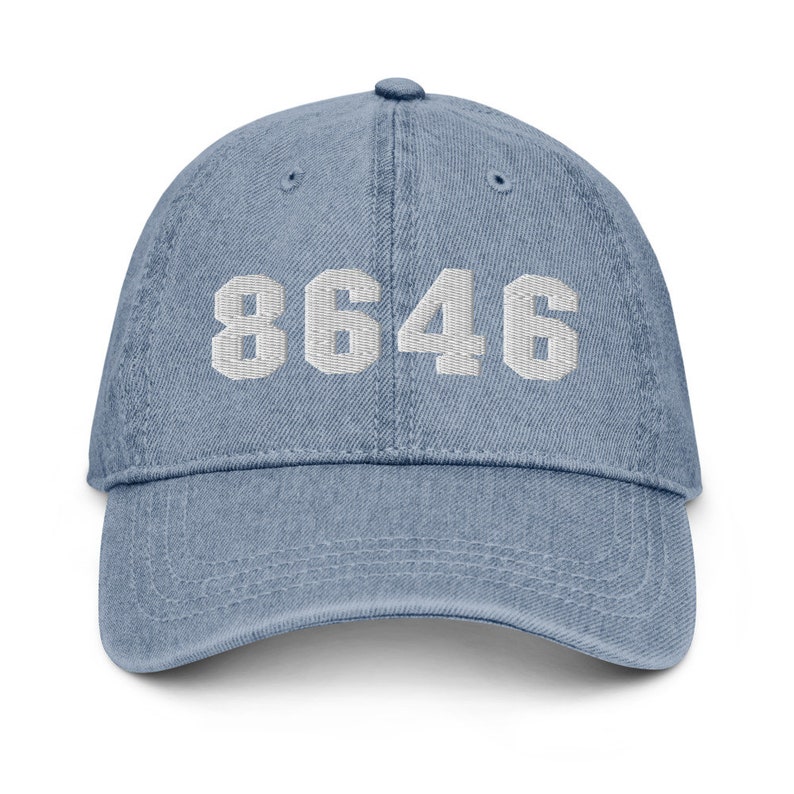 Puede incluir: Una gorra de b&eacute;isbol de mezclilla azul con texto blanco bordado que dice "8646".