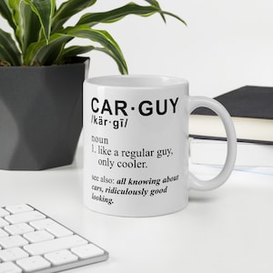 Op de afbeelding: Een witte keramische mok met zwarte tekst die "CAR-GUY /kär.gi/ zelfstandig naamwoord 1. als een normale kerel, alleen cooler. zie ook: alles weten over auto's, belachelijk goed uitzien."