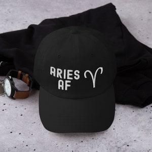 Könnte beinhalten: Schwarze Baseballkappe mit weiß gesticktem Text "Aries AF" und einem weißen gestickten Widdersymbol.