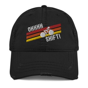 Könnte beinhalten: Schwarze, abgenutzte Baseballkappe mit einem weißen gestickten Design eines Fahrrads mit dem Text "OHHHH SHIFT!" im Retro-Stil mit roten, orangen und gelben Streifen.
