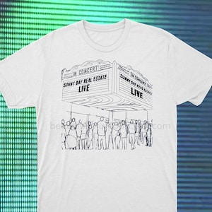 Puede incluir: Una camiseta blanca con una ilustración en blanco y negro de un lugar de conciertos con un cartel que dice "En concierto! Sunny Day Real Estate Live".