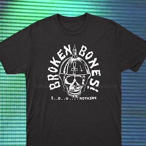 May include: Black t-shirt featuring a white graphic of a skull wearing a helmet with a cross on top. The text "BROKEN BONES" is in a circle around the skull. The text "I...D...U...NOTHING" is below the skull.