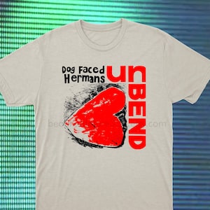 Op de afbeelding: Een lichtgrijs T-shirt met een rood hart en de tekst "Unbend" en "Dog Faced Hermans" gedrukt op de voorkant.