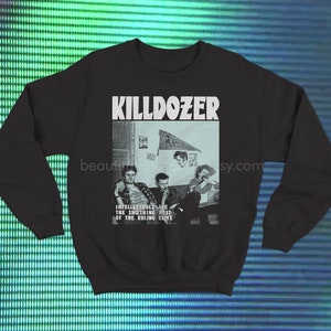 Puede incluir: Sudadera negra con la palabra "KILLDOZER" en blanco. Debajo, una imagen en blanco y negro de cuatro personas. El texto "INTELLECTUALS ARE THE MOONSHINE BOYS OF THE RULING ELITE" está impreso debajo.