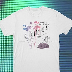 May include: White t-shirt with a graphic print of stylized flowers and the text "blood brothers crimes I believe in us" in black and pink.