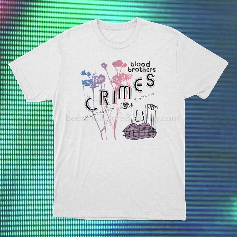 May include: White t-shirt with a graphic print of stylized flowers and the text "blood brothers crimes I believe in us" in black and pink.
