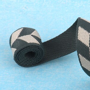 May include: A close-up of a rolled up dark green and white patterned webbing strap. The strap has a geometric pattern of white squares on a dark green background.