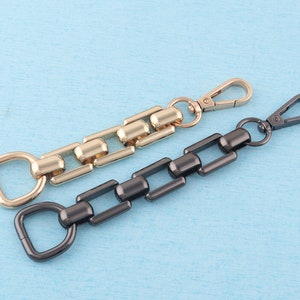 Peut inclure: Deux porte-clés en chaîne métallique, l'un doré et l'autre noir. Le porte-clés doré a une boucle à une extrémité et un anneau en D à l'autre. Le porte-clés noir a un mousqueton à une extrémité et un anneau en D à l'autre.