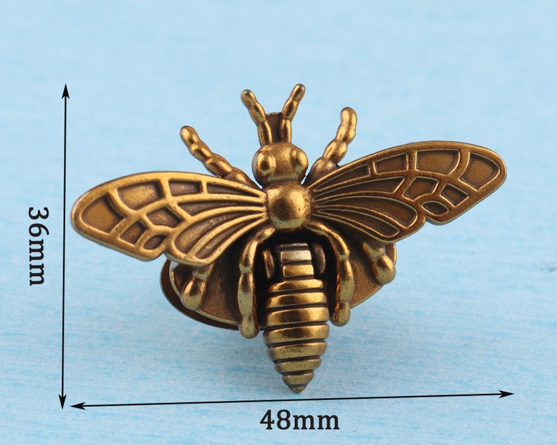May include: A gold-toned metal bee figurine with detailed wings and a textured body. The bee is approximately 4.8 inches wide and 3.6 inches tall.