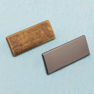 May include: Two rectangular metal plates, one gold and one black, with a textured surface.