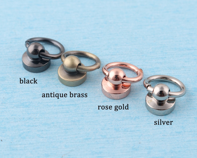 May include: Four metal rings with a ball in the center, each ring is a different color: black, antique brass, rose gold, and silver.