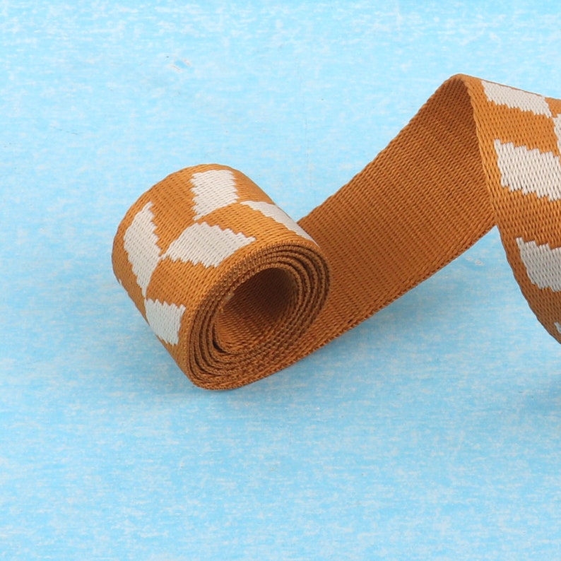 May include: A roll of brown and white patterned webbing. The webbing is woven with a white geometric pattern on a brown background.