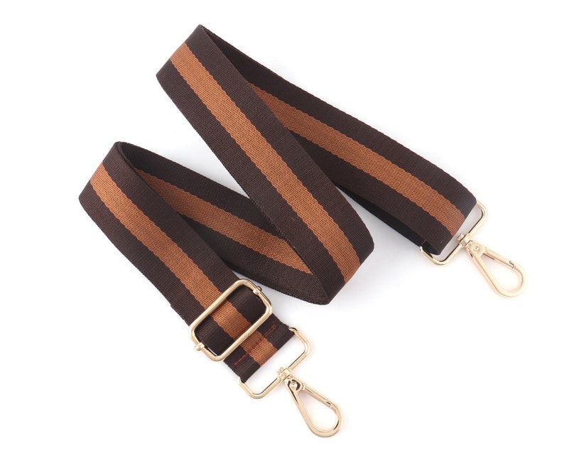 Pode incluir: Uma correia ajust&aacute;vel com listras marrons e bege e ferragens de metal dourado. A correia &eacute; feita de tecido tecido e tem um visual casual.